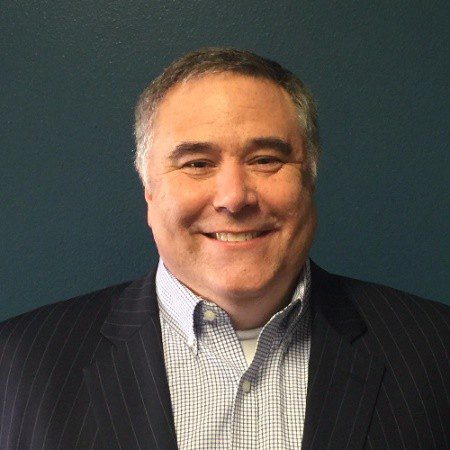 Smiling middle-aged man in a suit jacket against a dark background.