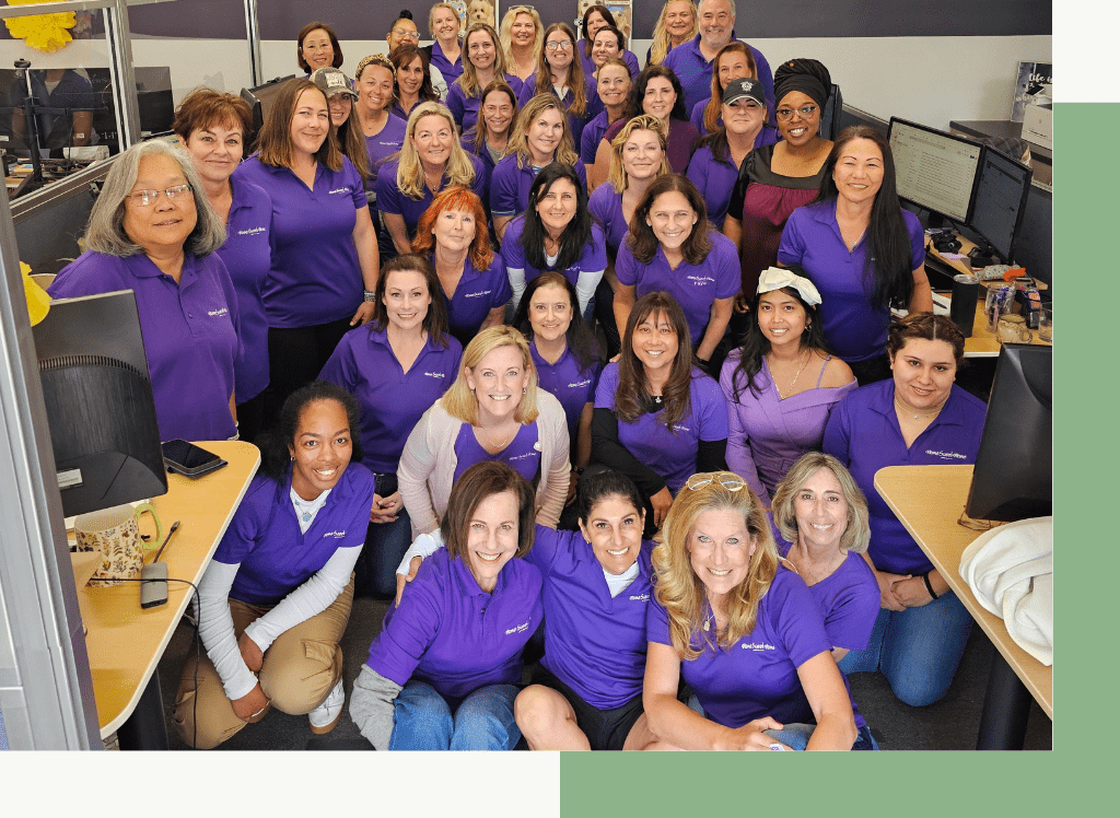 Group of women wearing purple shirts, smiling and posing together indoors.